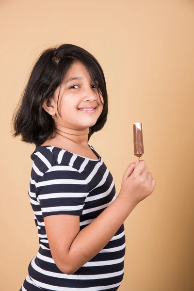 Indian girl eating ice cream or ice candy, asian girl and ice cream or ice candy, isolated on brown background, ten year old indian girl enjoying ice cream