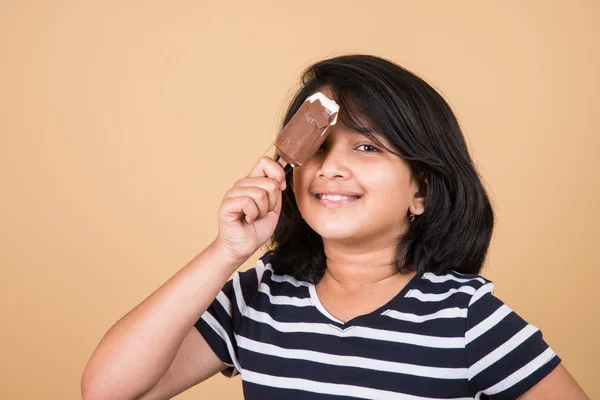 Indian girl eating ice cream or ice candy, asian girl and ice cream or ice candy, isolated on brown background, ten year old indian girl enjoying ice cream