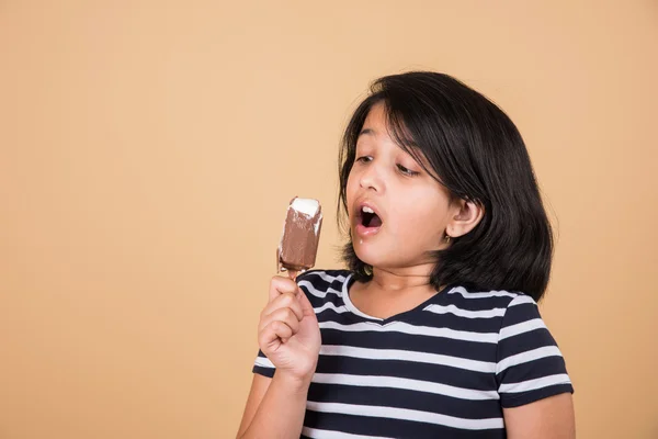 Indian girl eating ice cream or ice candy, asian girl and ice cream or ice candy, isolated on brown background, ten year old indian girl enjoying ice cream