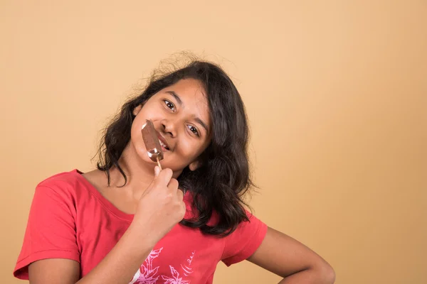 Indian girl eating ice cream or ice candy, asian girl and ice cream or ice candy, isolated on brown background, ten year old indian girl enjoying ice cream