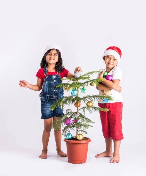 Indian little boy and indian little girl standing near decorated christmas tree showing happiness on their face, asian kids and christmas tree, isolated on white background