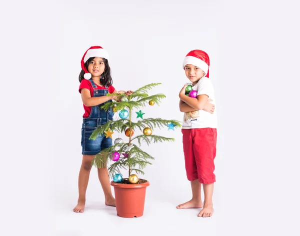 Indian little boy and indian little girl standing near decorated christmas tree showing happiness on their face, asian kids and christmas tree, isolated on white background