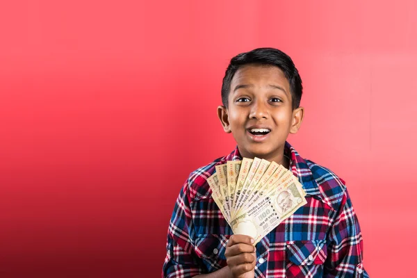 Indian kid holding currency notes, indian kid and money, indian kid with 500 rupee note fan, indian kid holding currency note fan,five hundred rupee notes, amazed, happy, front profile, red background