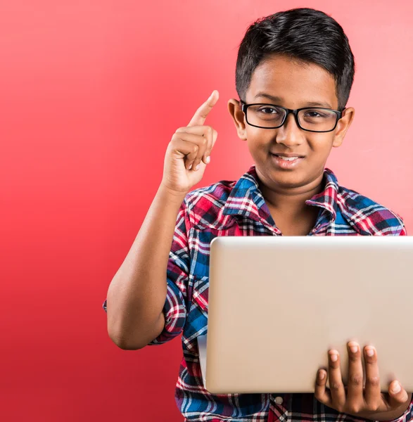 10 year old indian kid holding white laptop in hand, posing over red background, sitting or standing, indian kid with glasses and laptop, asian kid with laptop, smiling, confident