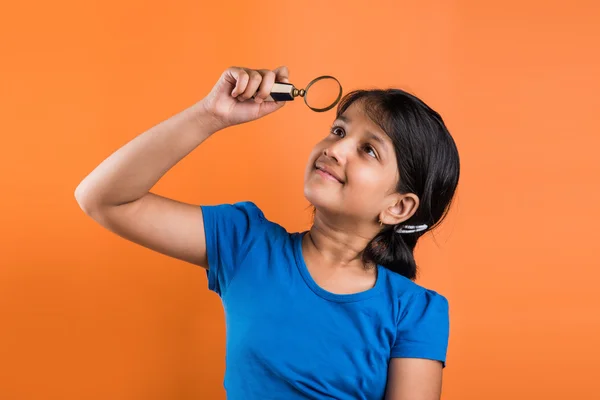 Cute little indian girl looking upwards through magnifying glass, indian girl with magnifying glass, asian girl with magnifying glass, isolated over orange background