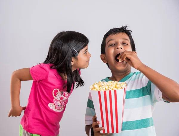 Asian little boy and girl watching movie with pop corn, little indian girl sitting with brother watching movie eating popcorn, indian kids eating pop corn, kids watching movie with pop corn