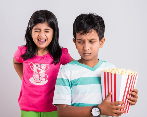 Asian little boy and girl watching movie with pop corn, little indian girl sitting with brother watching movie eating popcorn, indian kids eating pop corn, kids watching movie with pop corn