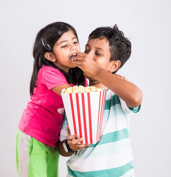 Asian little boy and girl watching movie with pop corn, little indian girl sitting with brother watching movie eating popcorn, indian kids eating pop corn, kids watching movie with pop corn