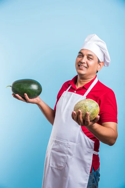 Handsome indian male chef holding water melon and musk melon, asian male chef holding fruits, isolated over blue background
