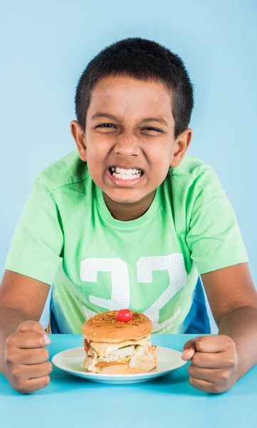 Cute indian boy eating burger, small asian boy and burger, over blue background