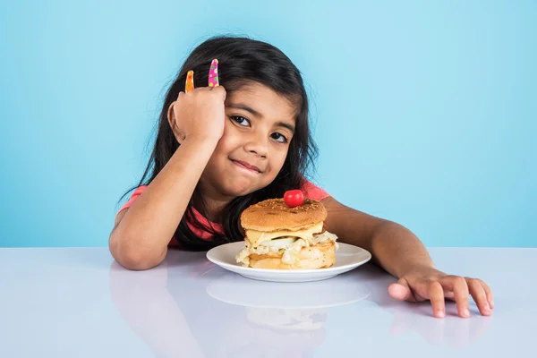 Cute indian girl eating burger, small asian girl and burger, isolated over yellow background