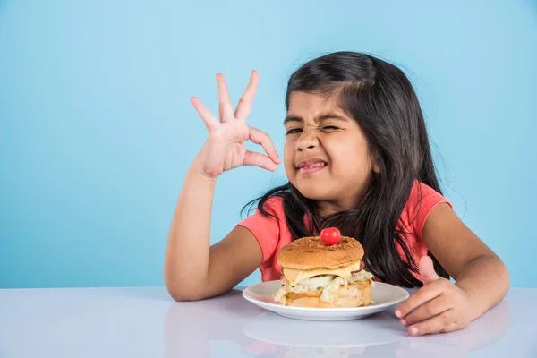 Cute indian girl eating burger, small asian girl and burger, isolated over yellow background