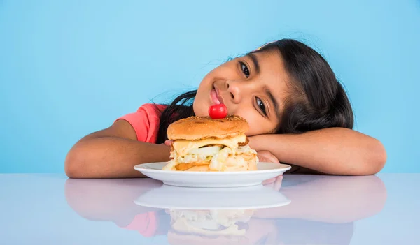 Cute indian girl eating burger, small asian girl and burger, isolated over yellow background