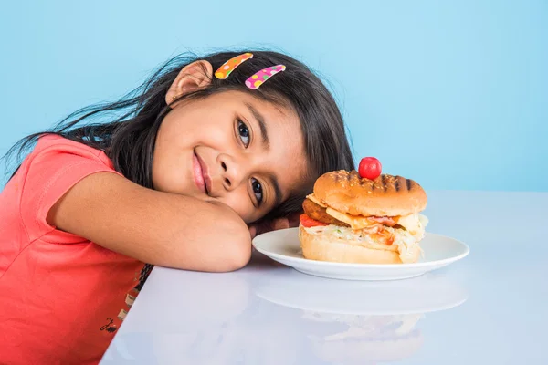 Cute indian girl eating burger, small asian girl and burger, isolated over yellow background