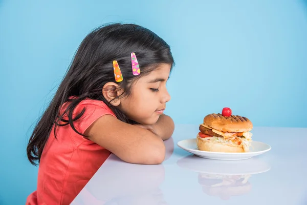 Cute indian girl eating burger, small asian girl and burger, isolated over yellow background