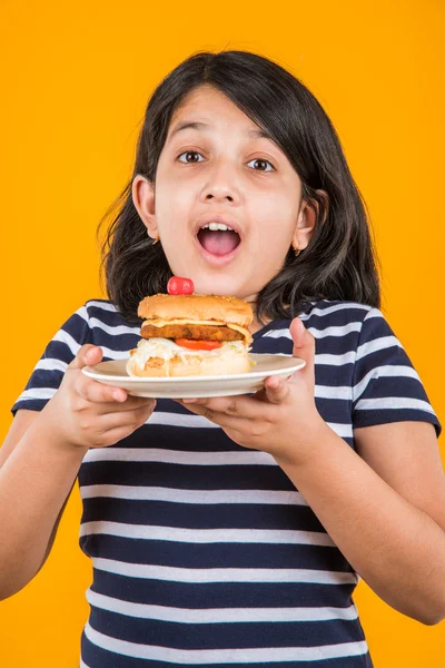 Cute indian girl eating burger, small asian girl and burger, isolated over colourful background