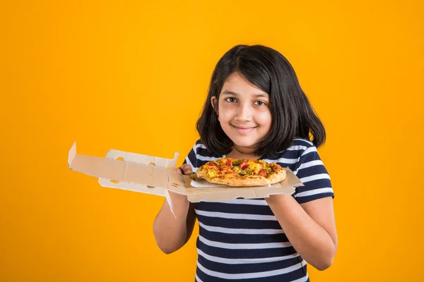 Portrait of cute indian girl holding an open box of pizza, excited asian girl opening pizza box showing smile on face, standing over yellow background