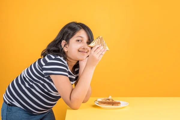 Indian girl eating sandwich, asian girl and sandwich, cute indian girl posing with sandwich on yellow background