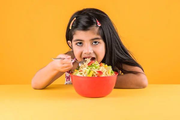 Happy Asian child eating delicious noodle, small indian girl eating noodles in red bowl