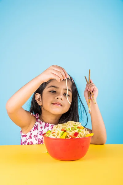 Happy Asian child eating delicious noodle, small indian girl eating noodles in red bowl