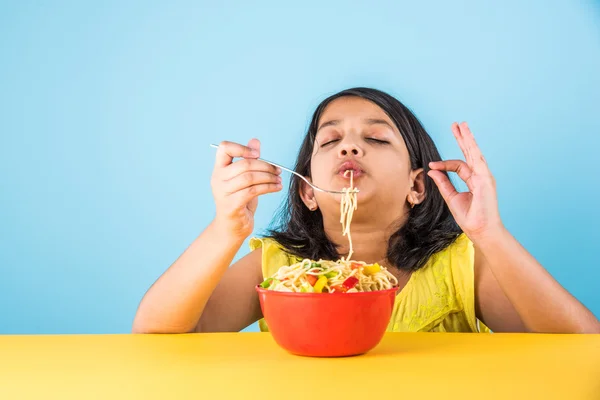 Happy Asian child eating delicious noodle, small indian girl eating noodles in red bowl, over blue background