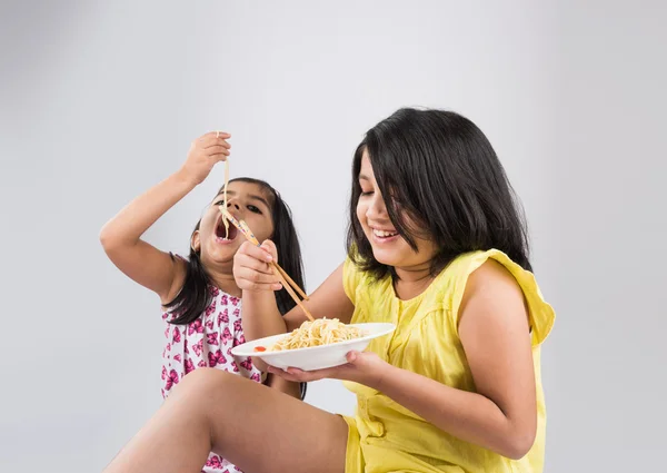 Happy Asian children eating delicious noodle, two cheerful little indian girls eating noodles in white dish isolated over white background