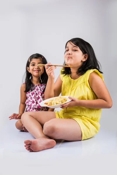 Happy Asian children eating delicious noodle, two cheerful little indian girls eating noodles in white dish isolated over white background