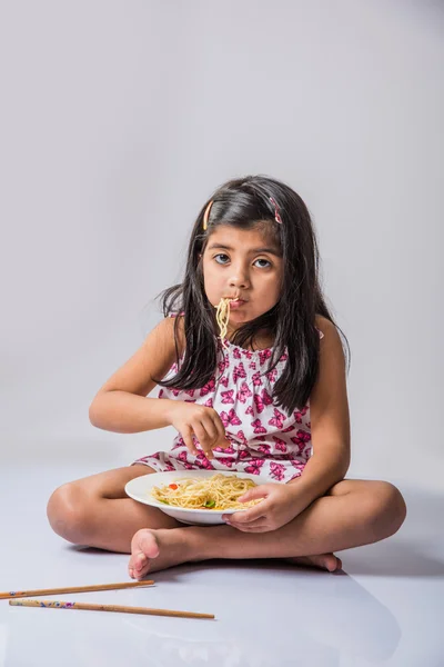 Happy Asian child eating delicious noodle, cheerful little indian girl posing with noodles in white dish isolated over white background, girl eating noodles