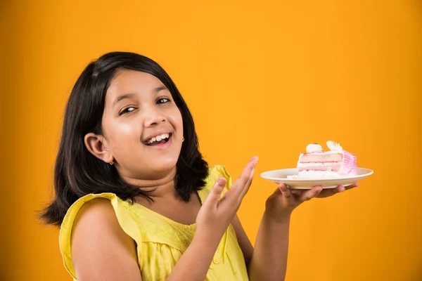 Portrait of Indian kid eating cake or pastry, cute little girl eating cake, girl eating strawberry cake over yellow background