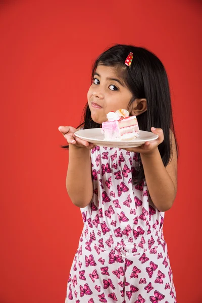 Portrait of Indian kid eating cake or pastry, cute little girl eating cake, girl eating strawberry cake over red background