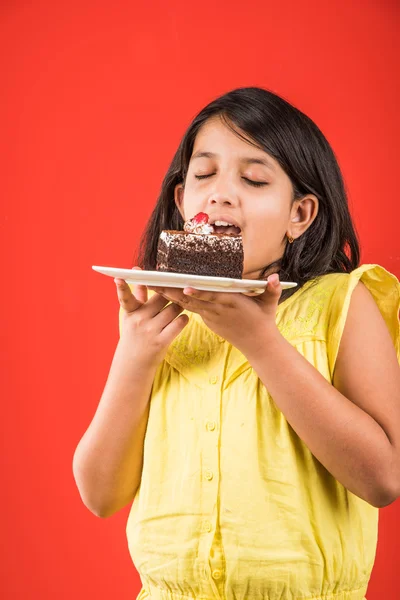 Portrait of Indian kid eating cake or pastry, cute little girl eating cake, girl eating chocolate cake or pastry over colourful background