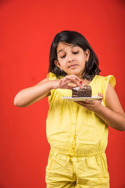 Portrait of Indian kid eating cake or pastry, cute little girl eating cake, girl eating chocolate cake or pastry over colourful background