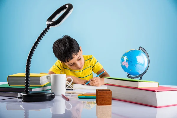 Indian small boy studying or doing home work, asian boy studying with coffee mug, globe model and books on table
