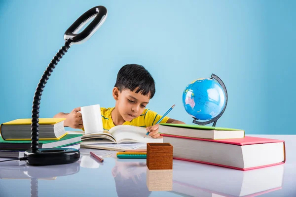 Indian small boy studying or doing home work, asian boy studying with coffee mug, globe model and books on table