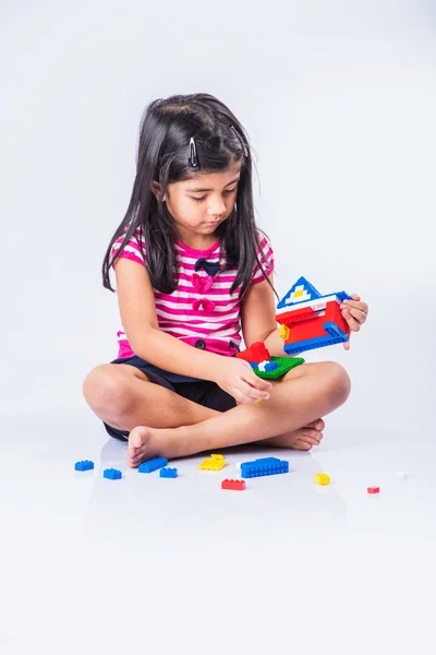 Indian small girl or asian girl child playing with colourful blocks over white background, cute little indian girl constructing house with blocks, cute indian girl playing with toys