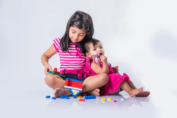 Indian small girls or asian small siblings playing with colourful blocks over white background, cute little indian girl baby sitting or taking care of younger sister, two small indian sisters playing