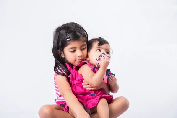 Indian small girls or asian small siblings playing with colourful blocks over white background, cute little indian girl baby sitting or taking care of younger sister, two small indian sisters playing