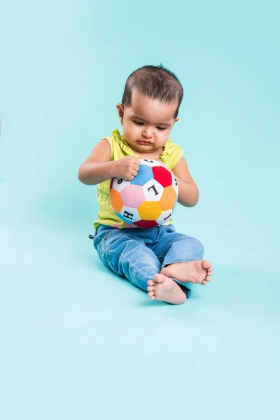 Indian baby girl playing with toys or blocks or soft toys over blue background, asian infant playing with toys, indian toddler playing indoor