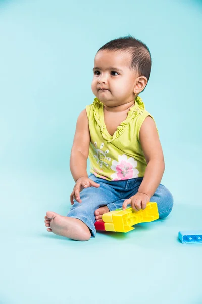 Indian baby girl playing with toys or blocks or soft toys over blue background, asian infant playing with toys, indian toddler playing indoor