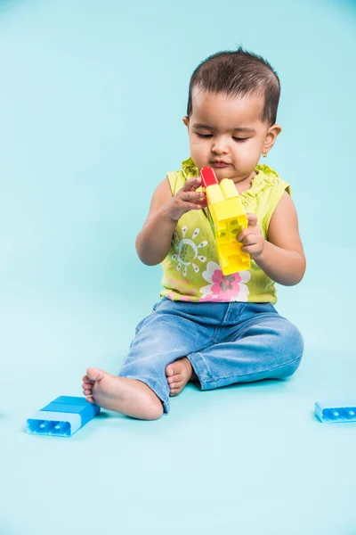 Indian baby girl playing with toys or blocks or soft toys over blue background, asian infant playing with toys, indian toddler playing indoor