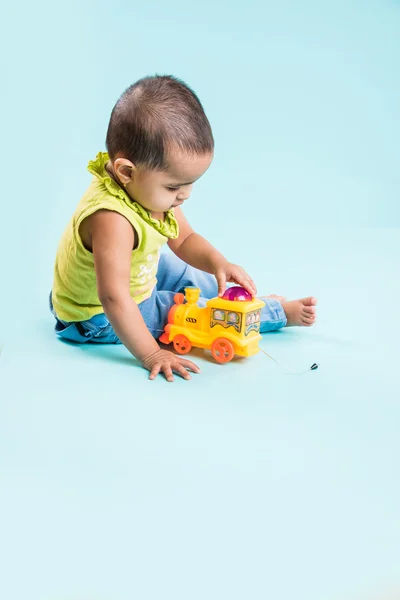 Indian child playing with colourful toy. Isolated on blue background, indian girl playing with engine toy, asian girl playing with colourful toy engine