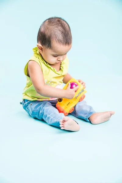 Indian child playing with colourful toy. Isolated on blue background, indian girl playing with engine toy, asian girl playing with colourful toy engine