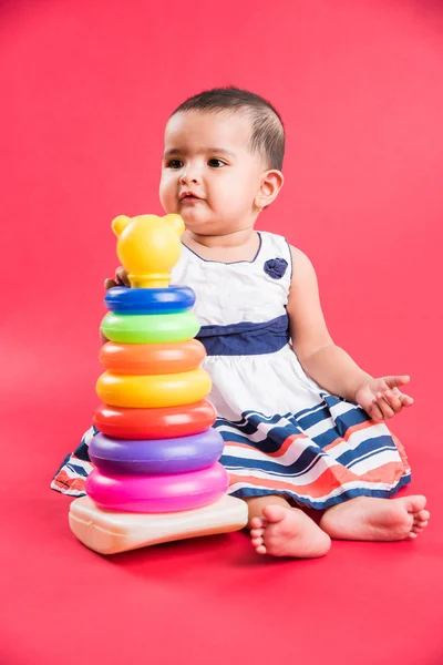 Baby Girl Stacking colorful Rings, Isolated over red, indian small girl playing with toy, asian baby girl playing with ring