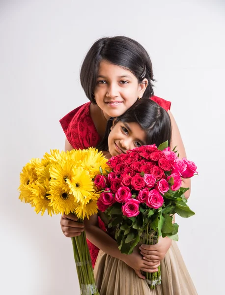 Two cute indian little girls holding flower bouquet, two small girls with gerbera and rose bouquet, isolated on white