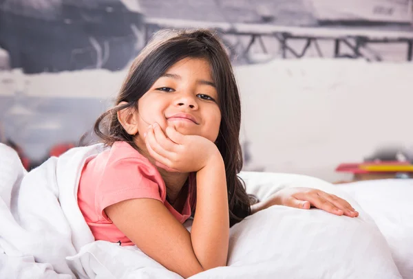 Adorable smiling indian little girl waked up in her bed or getting ready for bed happily, hands on chin