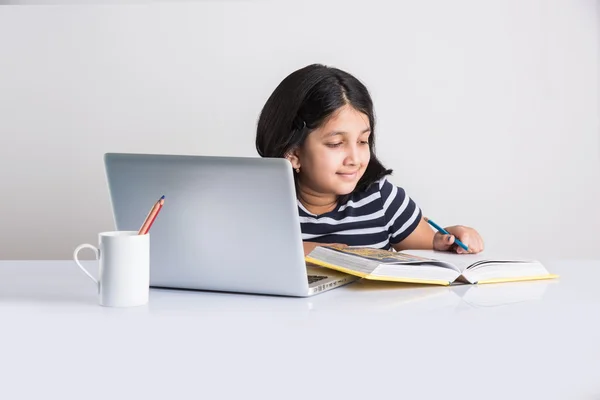 Cute little indian girl studying on laptop, asian small girl studying and using laptop, innocent indian girl child and study concept with pile of books & laptop