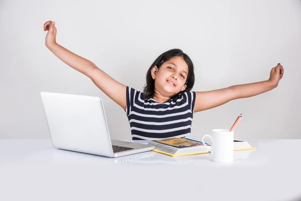 Cute little indian girl tired while studying on laptop, asian small girl studying on laptop and feeling sleepy, innocent indian girl childstretching hands while studying on laptop with pile of books