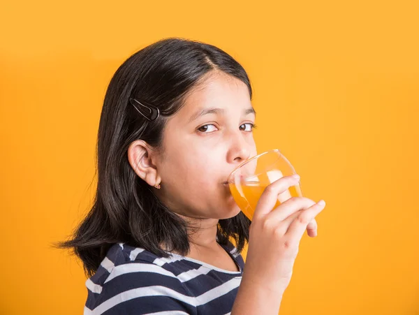 Portrait of indian small girl drinking mango juice or fruit juice in a glass, asian girl and a glass of juice, indian small girl holding a glass of mango juice or orange juice on yellow background
