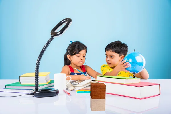 Indian kids studying geography and mathematics, small asian siblings studying, indian girl and boy doing homework on study table with globe, milk mug and pile of books, indian kids writing