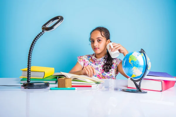 Education and home concept - stressed student girl with books, indian girl child tired of studying or doing homework, asian girl studying and stressed, with globe toy and coffee mug